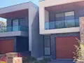 Nowoczesny bliźniak z cegły i betonu, z drewnianymi bramami garażowymi i szklanymi balustradami balkonów.