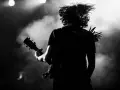 Muzyk z rozwianymi włosami gra na gitarze, w dymie i świetle sceny. Energia gatunku rockowego w czerni i bieli.