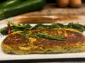 Polpettone di verdure dorato, guarnito con rosmarino, servito con contorno di verdure verdi e peperoncino.