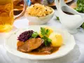 Deftiger Schweinebraten mit Klößen, Rotkohl und Sauerkraut. Dazu passt ein kühles Bier.