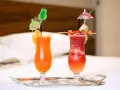 Dwa orzeźwiające drinki: jeden pomarańczowy z pomarańczą, drugi czerwony z truskawkami i ananasem, oba z parasolkami. Idealne na wakacje, może z dodatkiem triple sec.