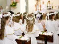 Dzieci w bieli, z wiankami na głowach, czekają na uroczystość. Piękne życzenia na komunie dla nich.