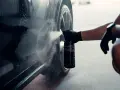 En hand med handske sprayar en bil för att ta bort dekaler.