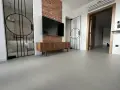 Nowoczesne wnętrze z betonową podłogą, co to jest mikrocement, która nadaje mu surowego charakteru. W tle widać łazienkę i salon.