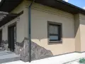 Elewacja domu w kolorze kawa z mlekiem, ozdobiona kamiennym cokołem. Widoczne okna i drzwi tarasowe.