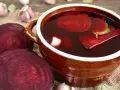 Głęboki, rubinowy zakwas z buraka w glinianym naczyniu, obok świeże buraki i czosnek. Idealny na zdrowie!