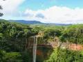 Majestatyczny wodospad na Mauritiusie spada kaskadami po skalnej ścianie, otoczony bujną, zieloną dżunglą i górami w tle.