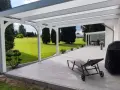 Moderne Terrasse bauen: Überdachter Sitzbereich mit Liegestuhl, Grill und Blick ins Grüne.