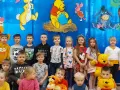 Dzieci pozują do zdjęcia z Kubusiem Puchatkiem i przyjaciółmi, świętując Dzień Kubusia Puchatka.
