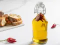 Olio al peperoncino in bottiglia, con peperoncini rossi e pane rustico a fette sullo sfondo.