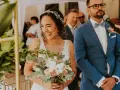 Szczęśliwa panna młoda z bukietem kwiatów i pan młody w niebieskim garniturze podczas ceremonii ślubnej.
