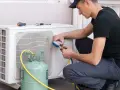 Técnico recargando gas aire acondicionado casa. Manómetro y tanque verde conectados a la unidad exterior.