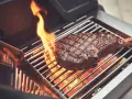 Ein saftiges Steak wird auf einem Gasgrill gegrillt, Flammen züngeln empor.