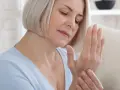 Kobieta zamyślona, masuje nadgarstek. Może to być jeden z objawów osteoporozy, który warto skonsultować z lekarzem.