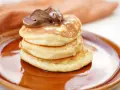 Stack of three fluffy American pancakes topped with chocolate spread on a brown plate.