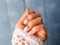Delikatne, jasnoróżowe paznokcie z kwiatowym zdobieniem. Nawet przy łamliwych paznokciach można stworzyć piękny manicure.