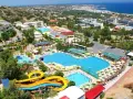 Widok z lotu ptaka na kompleks basenów z atrakcjami wodnymi i leżakami. Wiele osób korzysta z uroków słońca i wody. W tle widać budynki hotelowe i morze. Aqua Sun Village opinie potwierdzają, że to idealne miejsce na wakacje.