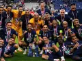 Un grupo de jugadores de Ligue 1 celebra con trofeos y medallas, sonriendo y vitoreando en el campo.