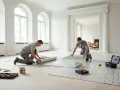 Due operai impegnati nella posa linoleum in un elegante salone con grandi finestre.