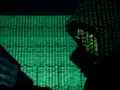 A hooded figure works on a laptop, bathed in the green glow of binary code. This scene evokes the shadowy world of China cyber espionage.