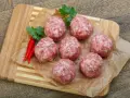 Surowe kotlety mielone keto, przyprawione papryczkami chili i natką pietruszki, leżą na papierze do pieczenia na desce.