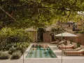 Piscina con galleggianti in un giardino rigoglioso, perfetto per idee piccoli giardini con piscina. Lettini e ombrellone invitano al relax.
