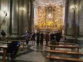 A group of people in a church, some holding hands, with a large golden altar in the background.