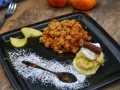 Ein köstlicher Apfel Crumble mit Haferflocken, serviert mit Vanilleeis, Sahne und einem Schokostäbchen.