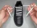 Mani che mostrano come mettere i lacci alle scarpe senza fiocco, con un laccio bianco che attraversa gli occhielli di una scarpa nera.