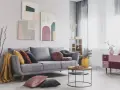 Divano grigio scuro con abbinamenti cuscini colorati e una coperta gialla. Tre quadri astratti decorano la parete.