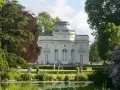 Un elegante edificio blanco con cúpula se alza en un exuberante jardin des plantes, con un estanque en primer plano y gente paseando.