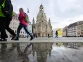 Menschen spazieren über einen nassen Platz vor der Frauenkirche, ein Symbol für offene Kirchen.