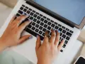 Mani che digitano su un laptop, forse per un corso di **università Pegaso**.