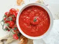 Ein Teller mit leuchtend rotem Sugo di Pomodoro, garniert mit einer einzelnen Kirschtomate. Daneben ein Bund frischer Tomaten und Zwiebeln.