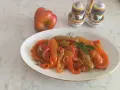 Piatto di peperoni alla siciliana, colorati e saporiti, con un peperone crudo sullo sfondo e saliere decorate.