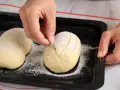 Eine Hand schneidet mit einem Messer Muster in ein mit Mehl bestäubtes Brot.