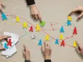 Ręce kierują kolorowymi ludzikami, tworząc ścieżki. To metafora rozwoju społecznego dziecka, gdzie interakcje kształtują jego drogę.