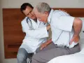 Lekarz bada starszego mężczyznę z bólem pleców, który może być objawem zespołu Munchausena.