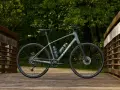 A grey Trek bike sits on a wooden bridge, ready for road or mountain biking adventures through the lush green forest.