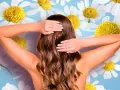 Mujer con cabello castaño ondulado, con las manos en la nuca, rodeada de margaritas. Un toque natural para aclarar el pelo con manzanilla.