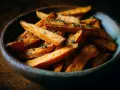 Un bol en bois rempli de frites de patate douce dorées et assaisonnées d'herbes.