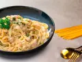Pasta cremosa con trozos de salmón y perejil, servida en un plato azul oscuro.
