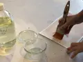 Application d'une finition acrylique sur une œuvre. Une main tient un pinceau large, prêt à recouvrir le papier d'une couche protectrice.