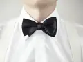 Elegancki mężczyzna w białej koszuli z czarną muszką i białymi szelkami. Kołnierzyk półwłoski idealnie dopełnia stylizację.