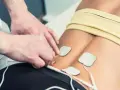 Fysioterapeut applicerar elektroder för elbehandling av muskler i ländryggen.