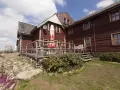 Drewniana szyprówka - chata pod sową, z werandą, stołami i krzesłami. W tle beczka i kamienista ścieżka.