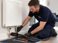 Instalator wykonuje wymianę grzejnika w bloku bez spuszczania wody, używając specjalistycznego sprzętu.