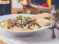 Pyszny makaron z sosem bolognese, posypany parmezanem i udekorowany bazylią. Czy to spaghetti, czy tagliatelle? Obok kromki chleba i kieliszek czerwonego wina.