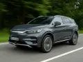 Szary BYD Tang jedzie po drodze, otoczony zielenią.