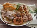 Un piatto invitante di grigliata di carne: costine, spiedini, salsicce e hamburger, guarniti con rosmarino fresco.